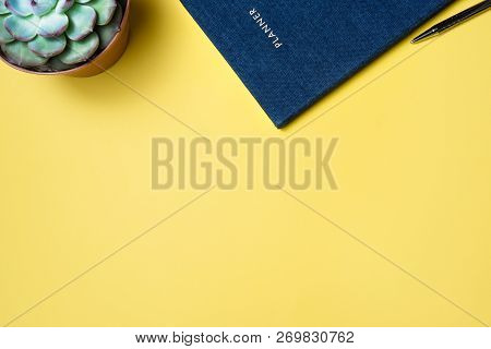 Flatlay Of Work Place Silver Laptop Secculent Plant And Blue Organizer Over Yellow Background