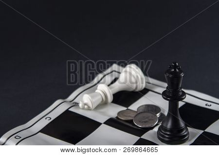 Two Chess Kings Standing In Front Of Each Other, Coins Between Them. White King Fallen. Strategy, Fi