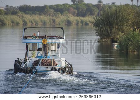 Small Tug Boat Towing A Yacht On Nile River In Egypt Through Rural Countryside Landscape