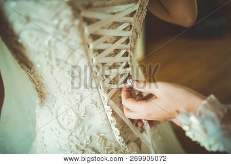 Bridesmaid Preparing Bride For The Wedding Day. Bridesmaid Helps Fasten A Wedding Dress The Bride Be