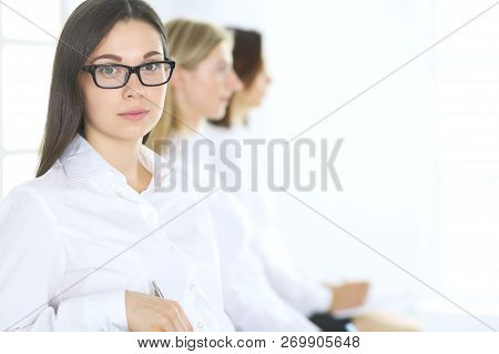 Attractive Businesswoman At Meeting Or Conference Against The Background Of Colleagues. Group Of Bus