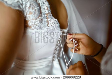 Bridesmaid Preparing Bride For The Wedding Day, Helps Fasten A Wedding Dress The Bride Before The Ce