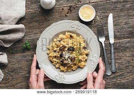 Barley Mushrom Risotto On Plate Over Rustic Wooden Background With Person Holding A Plate And Vintag