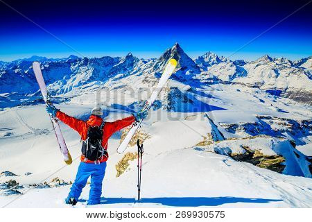 Man skiing on fresh powder snow. Ski in winter season, mountains and ski touring backcountry equipments on the top of snowy mountains in sunny day with Matterhorn in background, Zermatt in Swiss Alps.