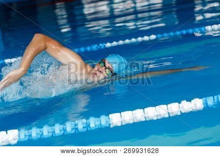 Image of sportsman in blue cap swimming in style of crawl in swimming pool