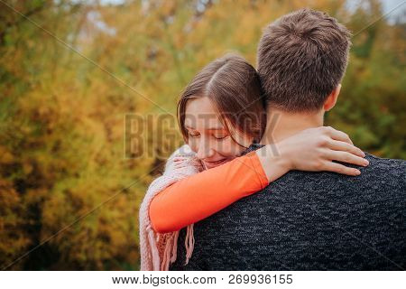 Young Woman Stand And Ebrace Man. She Holds Her Head On His Forehead. They Are In Park.