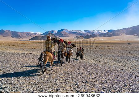 Mongolian Eagle Hunter In Tradition Clothes On Horseback Riding To The Golden Eagle Festival Competi