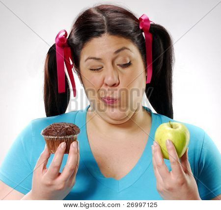 En ung fedt kvinde holder en chokoladekage og apple.