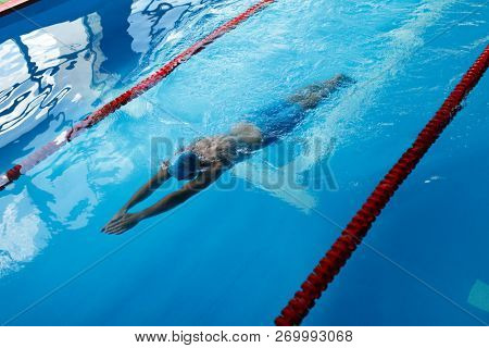 Photo of athlete man in blue cap swimming on path in pool