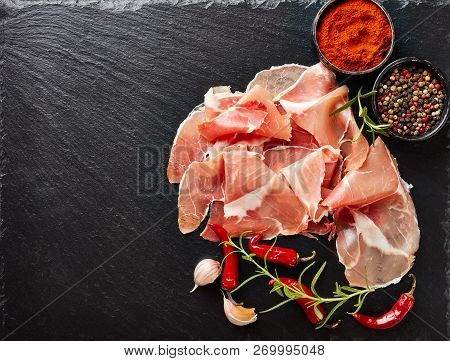 Spanish Dry-cured Ham, Jamon Curado Thinly Sliced And Served On A Black Stone Plate With Rosemary An
