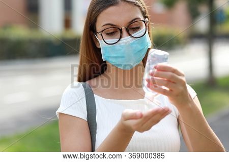 Portrait Of Young Woman With Surgical Mask Using Hand Sanitizer Gel In City Street. Antiseptic, Hygi