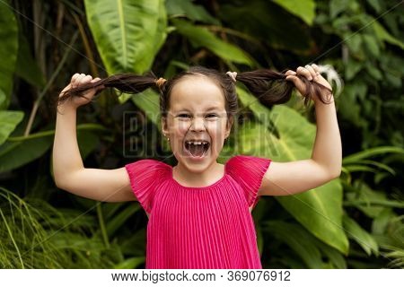 A Beautiful Girl In A Bright Dress Holds Two Tails Of Hair And Pulls It To The Sides And Smiles