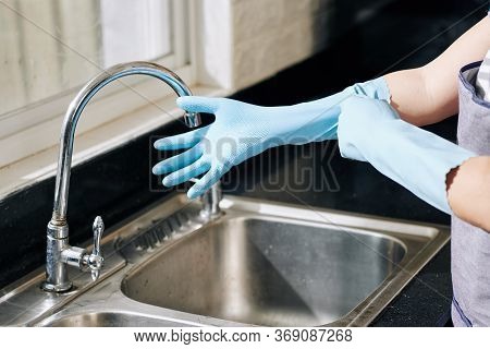 Hands Of Housewife Putting On Rubber Gloves Before Cleaning Surfaces In Kitchen