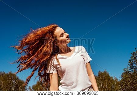 Young Happy Girl With Flying Long Curly Hair In Sunshine. Sky Background.