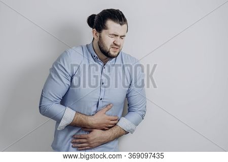 A Guy With Curly Hair Clings To His Stomach. Discomfort Of A Health Problem