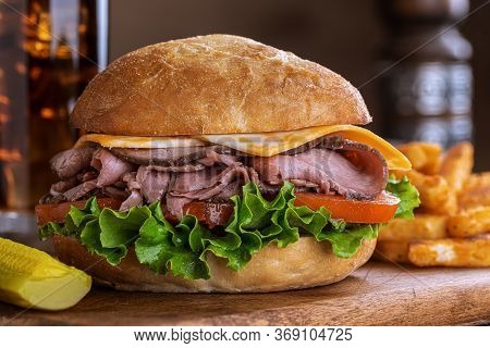 Roast Beef Sandwich With Cheese, Tomato And Lettuce On A Bun On A Wooden Cutting Board