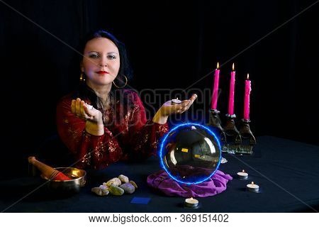 Young Clairvoyant And Fortune Teller With Candles In Hands In A Magic Salon On A Black Background.
