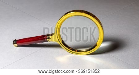 Close Up Single Golden Magnifying Glass Loupe With Red Wooden Handle, Leaning On The Gray Table With