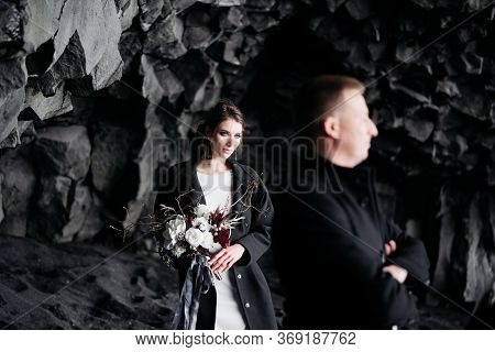 Destination Iceland Wedding. Wedding Couple Under A Rock Of Basalt Stones. Bride And Groom On The Bl