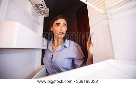 Coronacrisis Concept. Shocked Girl Looking At Her Empty Fridge Shelves In Despair, View From Inside