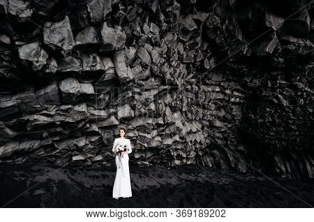 Destination Iceland Wedding. The Bride In A White Silk Dress With A Bouquet In Her Hands, Stands On 