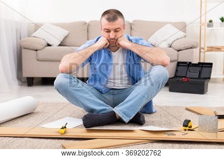 Furniture Assembly Trouble. Sad Man Sitting Near Disassembled Shelf Having Problems Installing Self-