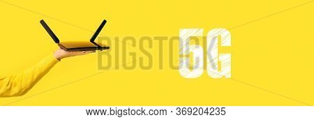 Black Wifi Router On Hand Over Yellow Background, 5g Concept, Panoramic Image