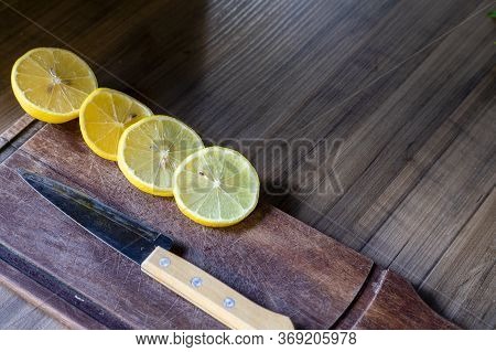 Some Slices Of Lemon Cut On A Wooden Board Next To A Knife On A Rustic Background