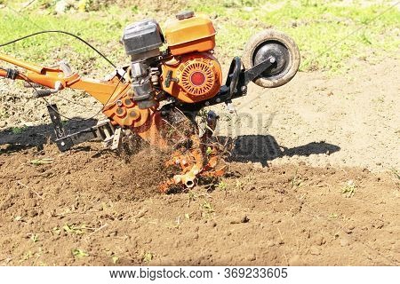 Man Farmer Plows The Land With A Cultivator. Agricultural Machinery: Cultivator For Tillage In The G