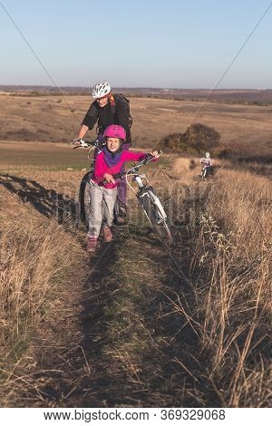 Mother And Kids On Their Bikes Go Up The Hill.
