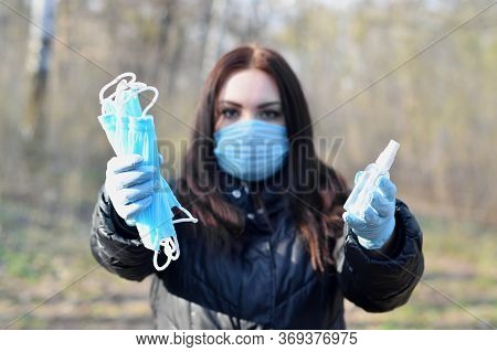 Young Woman In Protective Mask Shows Sanitizer Spray Bottles And Protective Face Masks Outdoors In S