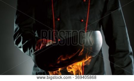 Closeup of chef holding empty wok pan in fire, ready to prepare for cooking.