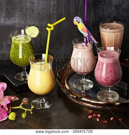 Smoothies composition on black marble table. Fresh creamy fruit beverages with straws. Summer non-alcoholic refreshment concoctions. Delicious healthy blended drinks. Nutritious protein breakfast