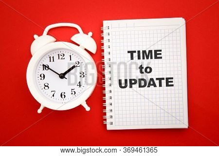 Top View Of Alarm Clock And Notebook With Time To Update On Red Background