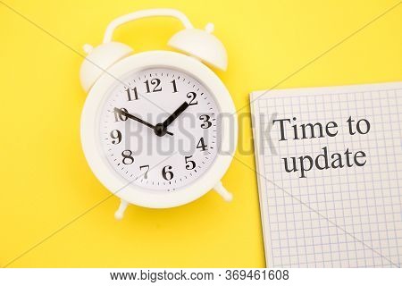 White Alarm Clock And Notebook With Time To Update On Yellow Background
