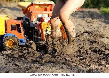 A Barefoot Child Jumping In A Puddle With Gras On A Summer Day. Baby Feet Stained With Goin. Brown S