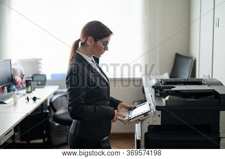 Business Woman In A Suit And Glasses Makes Copies Of Documents On A Photocopier. Female Office Manag