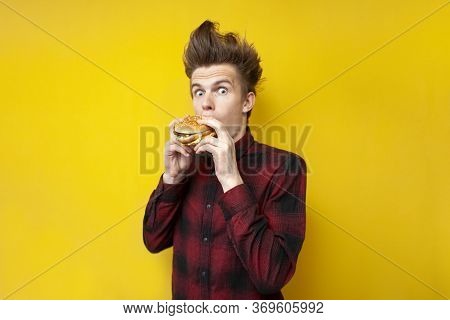 Shocked Guy Eating A Burger On A Yellow Isolated Background, Surprised Hipster Eating Tasty Fast Foo