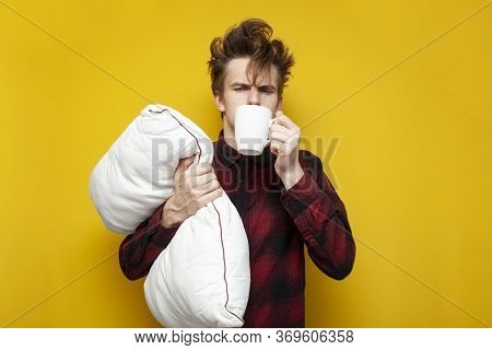 Sleepy Tired Guy Holds A Pillow And Drinks Coffee In The Morning On A Yellow Isolated Background, Ba