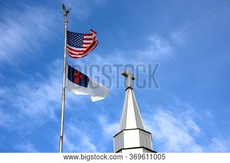 American And Christian Flag Fly Besides A Church Steeple With A Cross Symbol On Top.  Blue Skies And