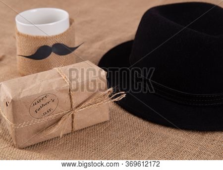 Gift Box On The Table. Next To A Cup With A Glued Mustache.