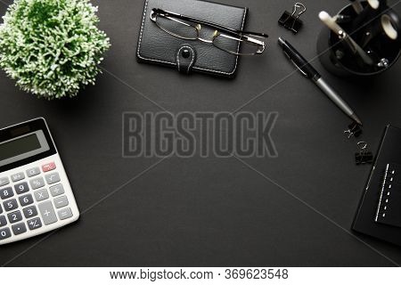 Top view of modern black office desk with calc, notebook, pen and a lot of things. Flat lay table layout. Copy space for text.