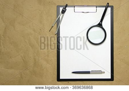 A Tablet With A White Sheet Of A4 Format With Magnifier, Pen And Divider On A Beige Craft Paper. Con