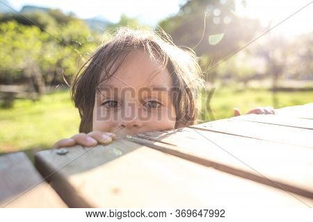 Smiling Boy Peeps From The Wooden Table, A Child Is Peeping From Behind A Wooden Fence, Portrait Of 