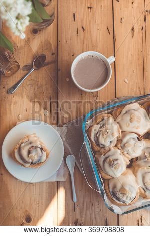 Freshly Baked Cinnabon Buns With Cream In A Glass Dish And A Cup Of Cocoa On A Wooden Table, Top Vie