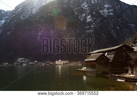 Halstatter Lake In Sun Rays Near Traditional Wooden Boat Houses And Against Mountains In Famouse Vil