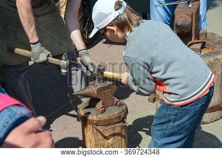 a boy helps a blacksmith make a horseshoe