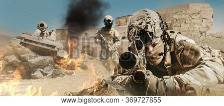 Photo of a fully equipped soldiers laying and aiming rifle on desert battlefield with running soldiers and tank.