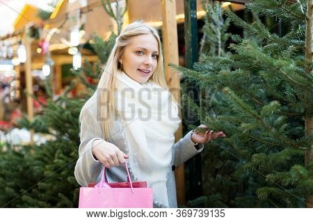 Happy Young Woman Inspecting Fir-trees At Christmas Market