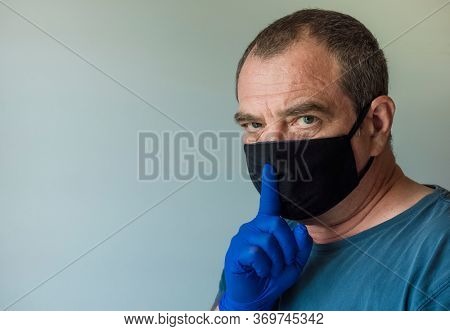 Adult man in a medical mask with a finger at his mouth. Coronavirus conspiracy theory concept